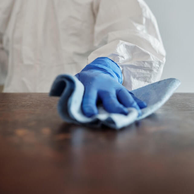 Close up of person wearing blue gloves and cleaning a table with a blue cloth