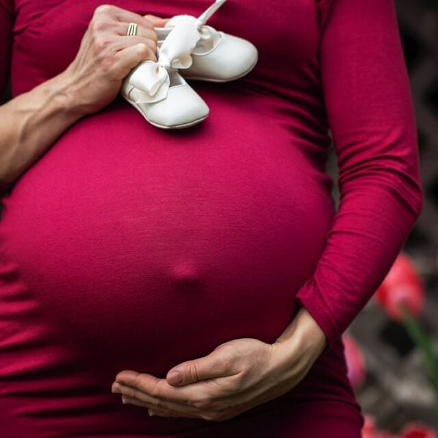 pregnant woman holding baby shoes